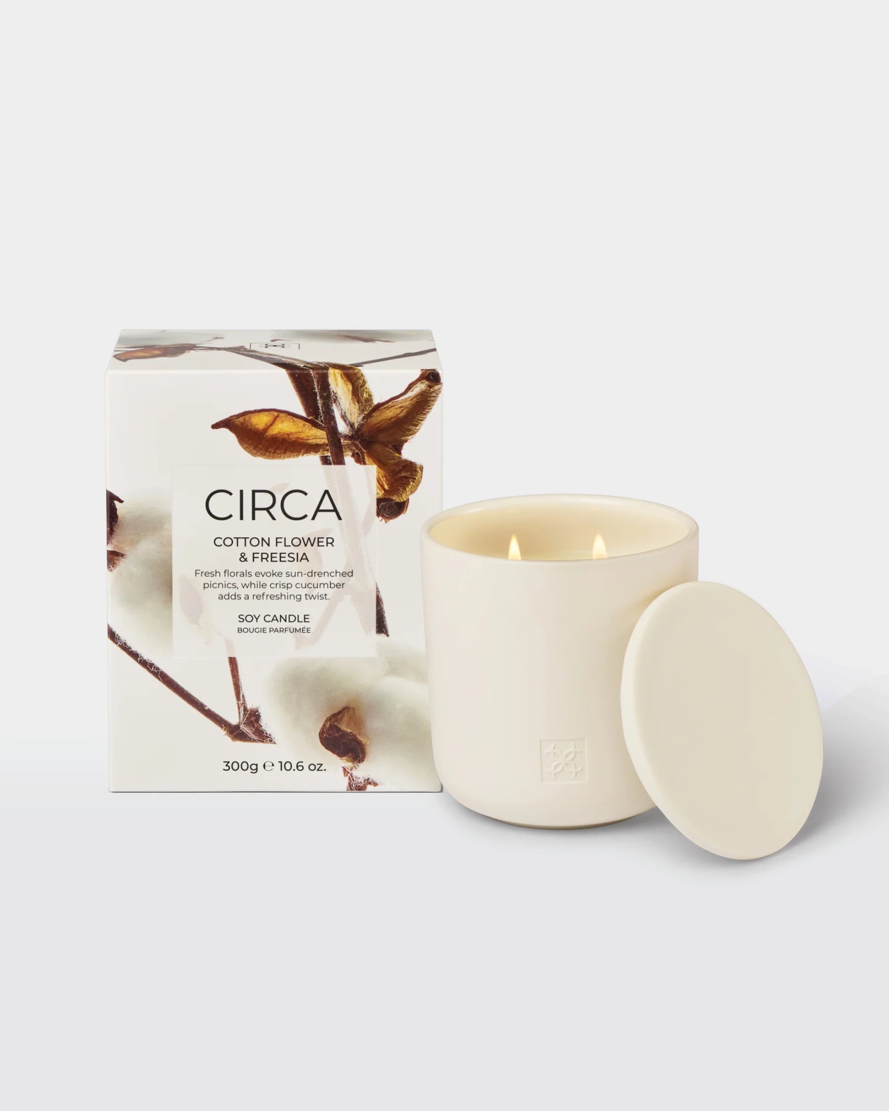 Soy candle in a glass jar with a cotton flower and freesia scent, 300g, from Circa, with a lit wick and floral decor.
