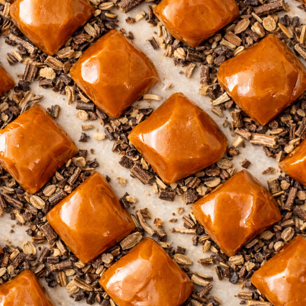 Golden liquorice caramel candies in a 100g New Farm package, showcasing soft caramel with liquorice flavor.